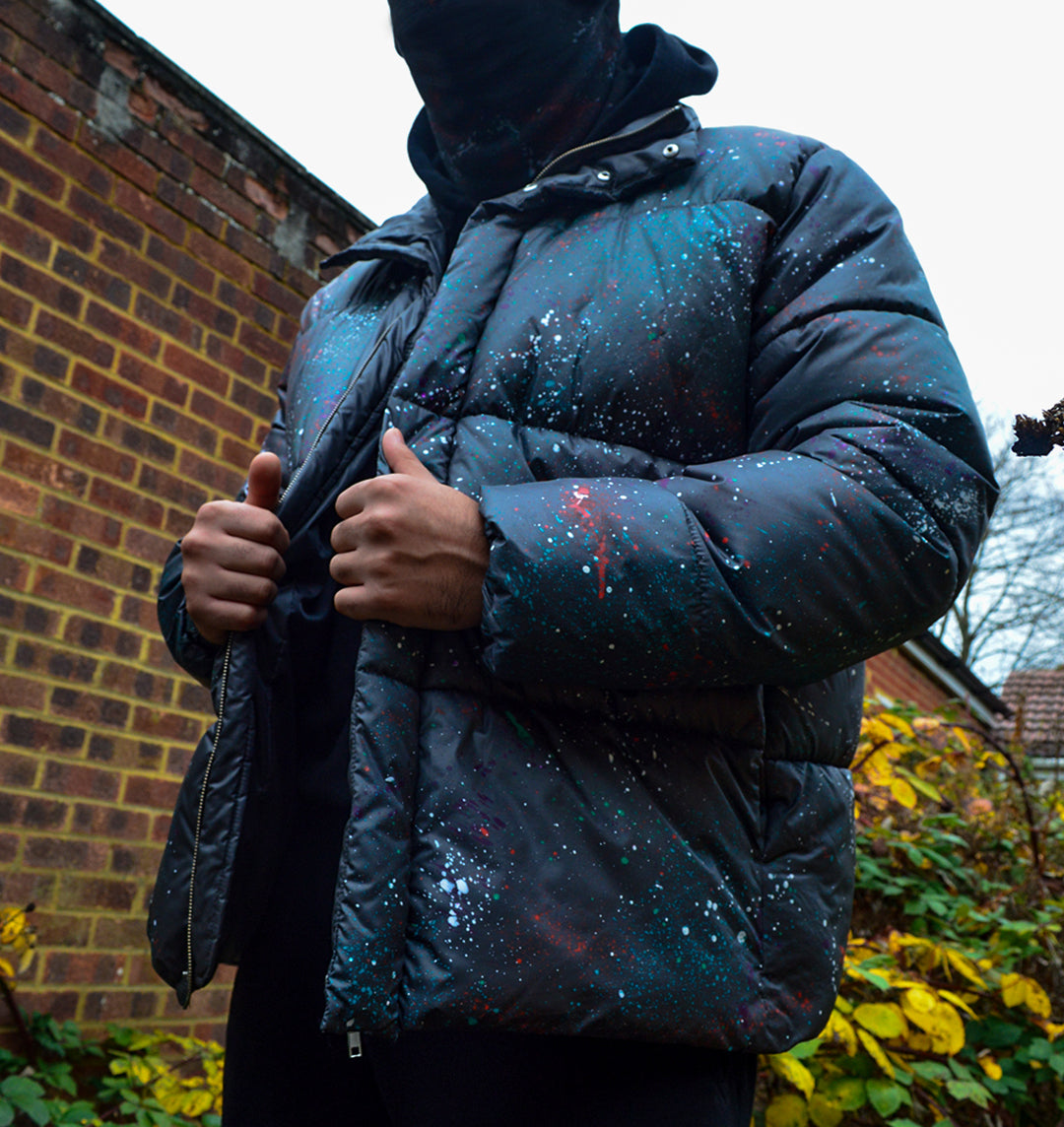 Upcycled puffer jacket in grey, with multi colour paint splatter across the whole thing