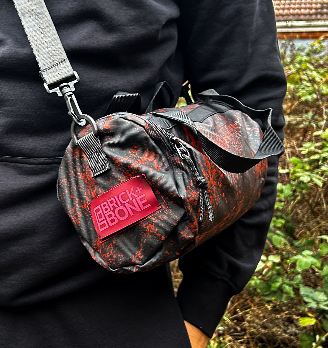 Black barrel bag with red paint splatter and red leather BRICK + BONE logo